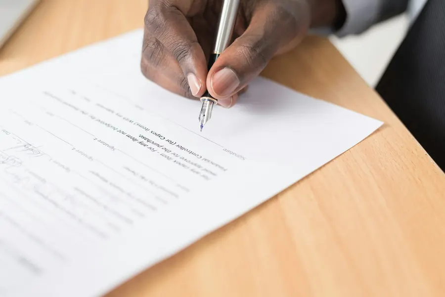 A hand signing a printed agreement with a fountain pen